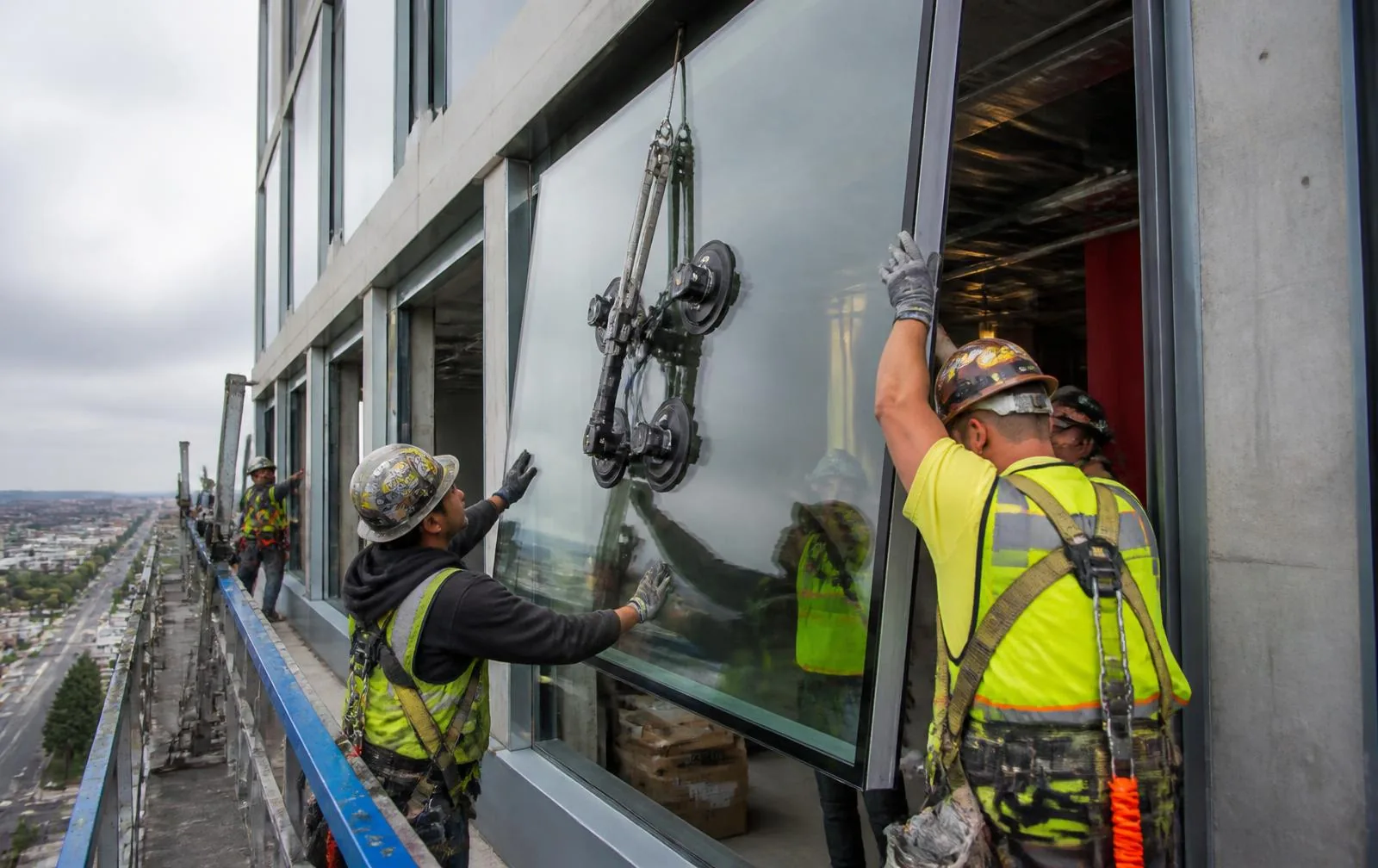 Glazing crew setting a large insulated glass unit into an aluminum curtain wall frame on a mid-rise building